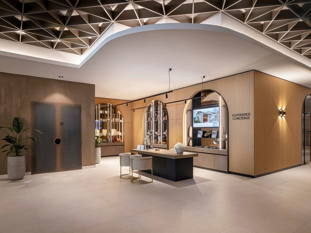 Concierge desk signed Experience Concierge in a lobby, with arched display shelving, a planted pot and an illuminated patterned ceiling.
