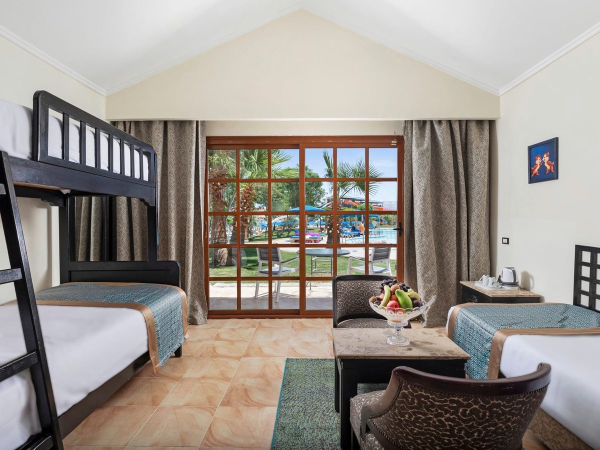 A family bungalow with black-framed bunk beds on one side, a single bed and armchairs on the other, and glass doors onto a garden terrace.