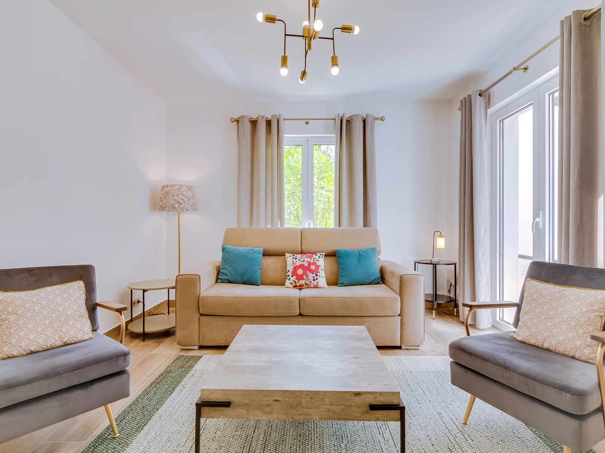 A townhouse living room with a beige sofa, two grey armchairs, a low coffee table and tall balcony doors.
