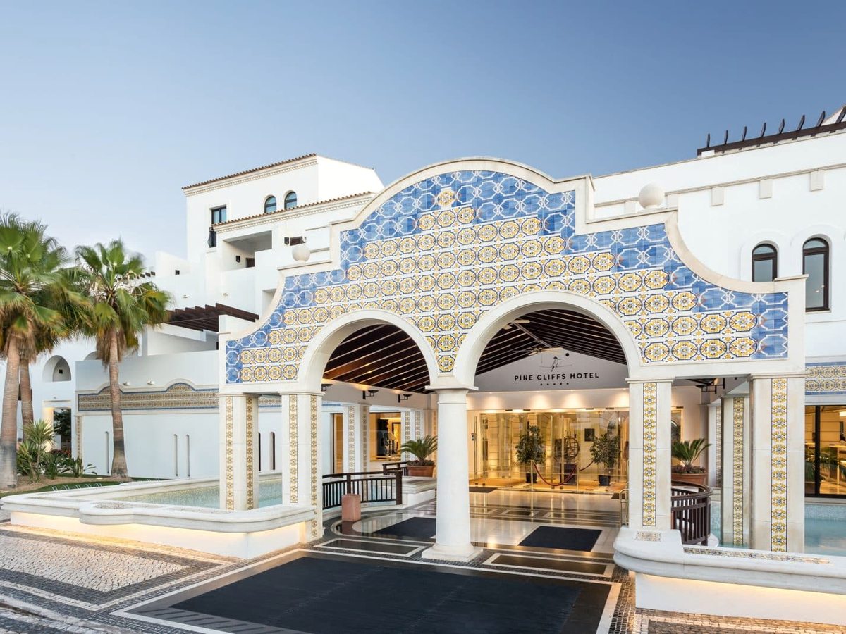 The hotel entrance, a tall white arch faced in blue and yellow azulejo tiles, with palms to one side and a lit lobby doorway beneath.