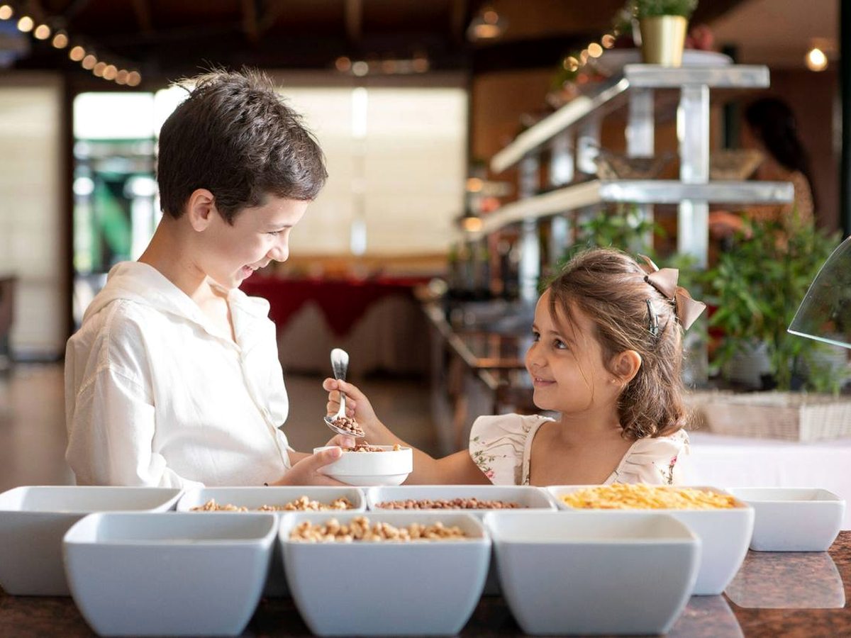 Two children helping themselves from white bowls of cereal, nuts and dried fruit at a buffet counter inside the restaurant.