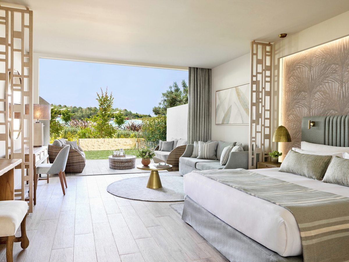 Open-plan suite with a large bed, a sofa and armchairs in the same room, and full-height glazing sliding back to a lawn and terrace.