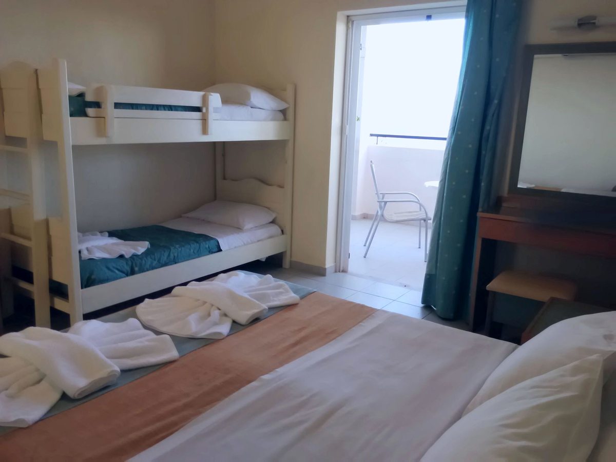 Bedroom with white wooden bunk beds beside a double bed, a dressing table and mirror, and open doors onto a balcony.