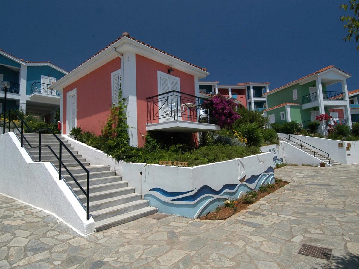 Pastel bungalow blocks with covered balconies above a stone-paved courtyard, with broad steps and a handrail leading up between them.