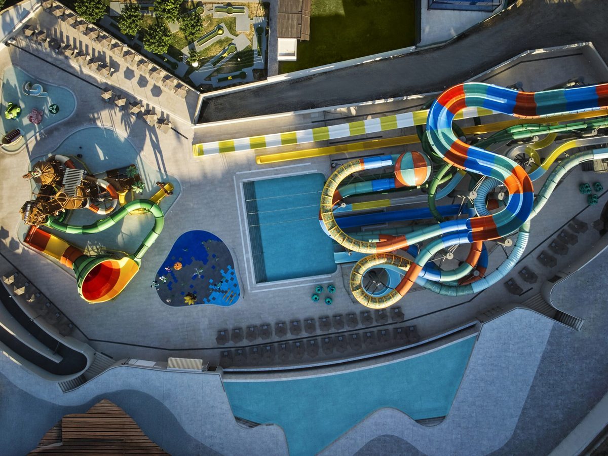 Overhead view of the waterpark, showing looping multicoloured slides, a timber play structure, a splash area and a rectangular pool.