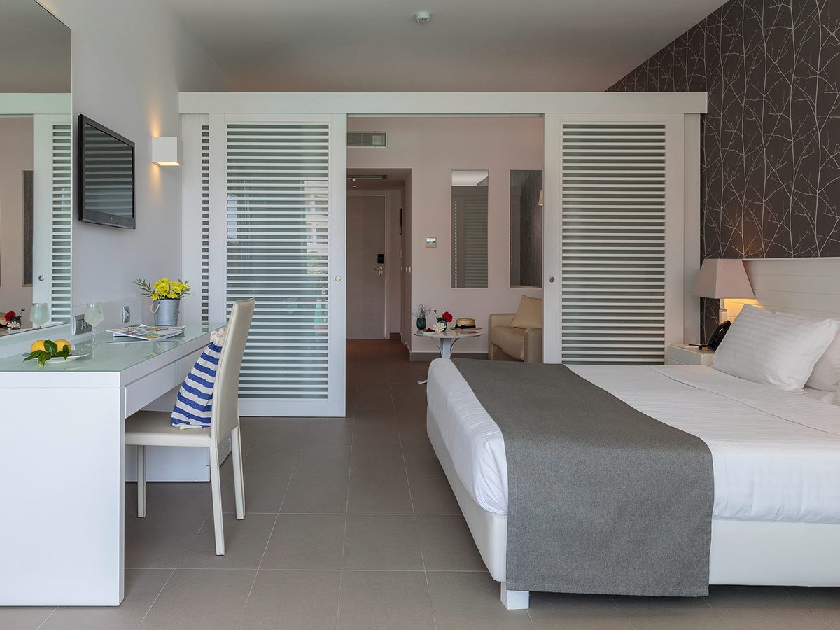 Ground-floor family room with a bed against a dark patterned wall and tall louvred sliding doors dividing it from the hallway and a seating area.