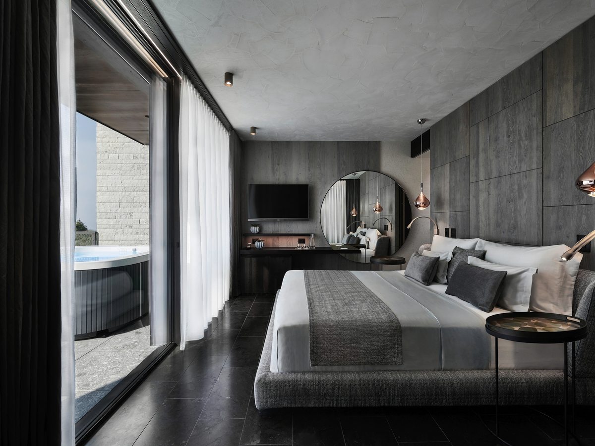 A grey-toned double room with a king-size bed, copper pendant lights and a round mirror, its sliding glass doors open to a private terrace with a whirlpool.