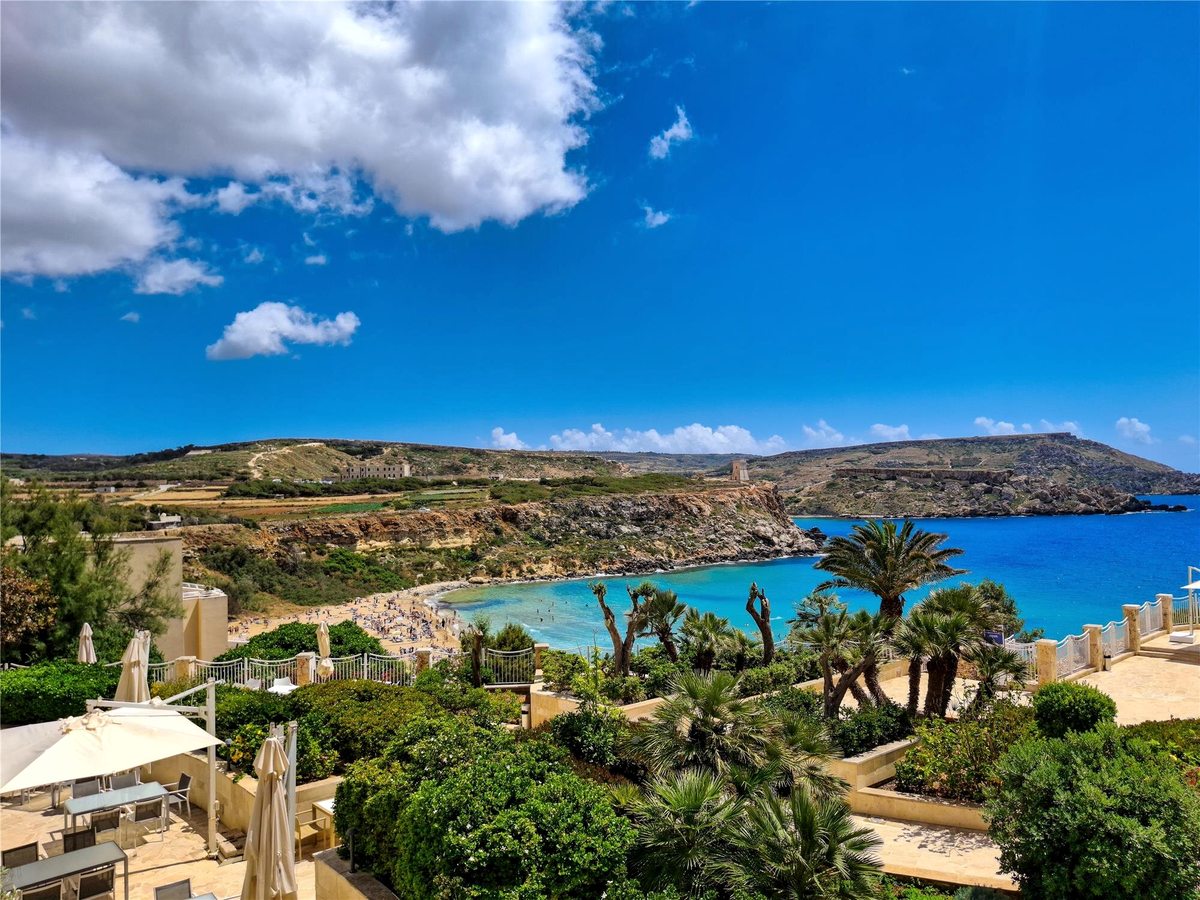 Golden Bay's crescent of sand with bathers in the shallows, beyond the resort's terraced gardens of palms and clipped shrubs, with headlands and countryside behind.