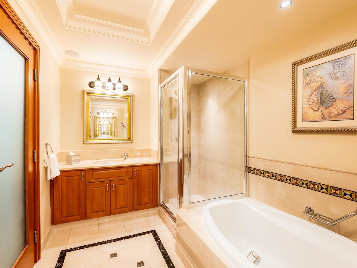 Bathroom with a cream marble surround, a wooden vanity unit and gilt mirror, a glass shower cubicle and a full-size bath.