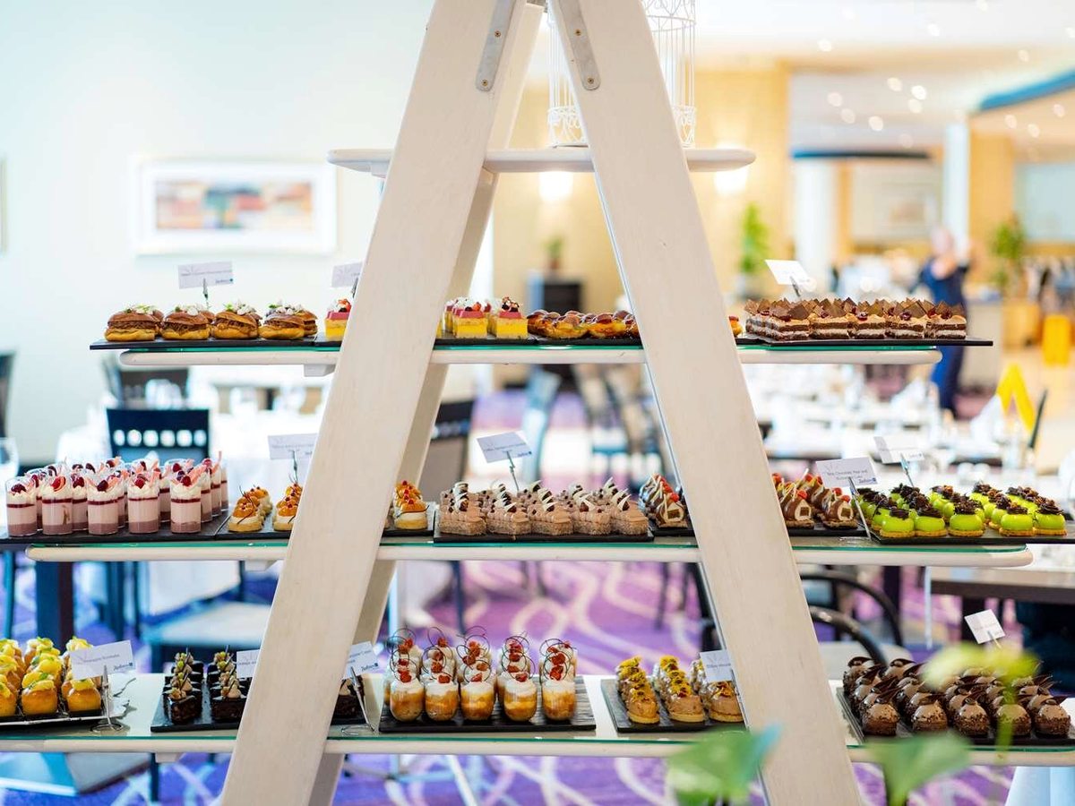 Stepped wooden display stand set with individual cakes, fruit tartlets and mousse cups on white plates.