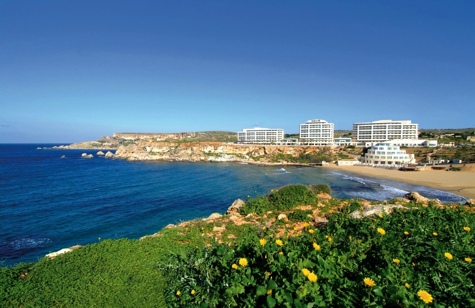 The Radisson Blu Golden Sands resort on the clifftop at the north end of Golden Bay, Malta, with the sandy beach below.