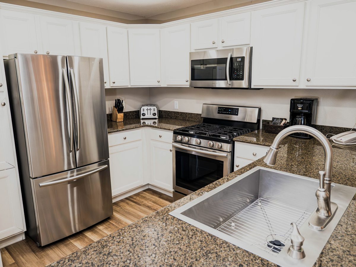 A villa kitchen with white cabinets, granite worktops, a central island with a sink, a French-door fridge-freezer, a gas hob and stainless-steel appliances.