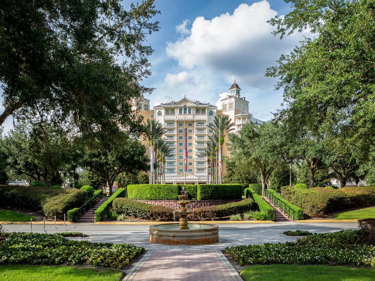 A formal garden with clipped hedges, a tiered fountain and a garden path, the resort tower rising behind under a blue sky.