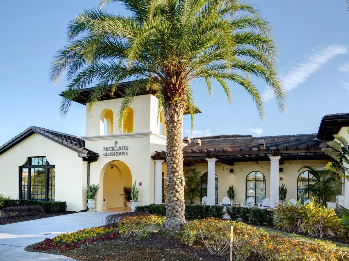A cream Mediterranean-style clubhouse with an arched entrance marked Nicklaus Clubhouse, a tiled roof, white columns and tropical planting.