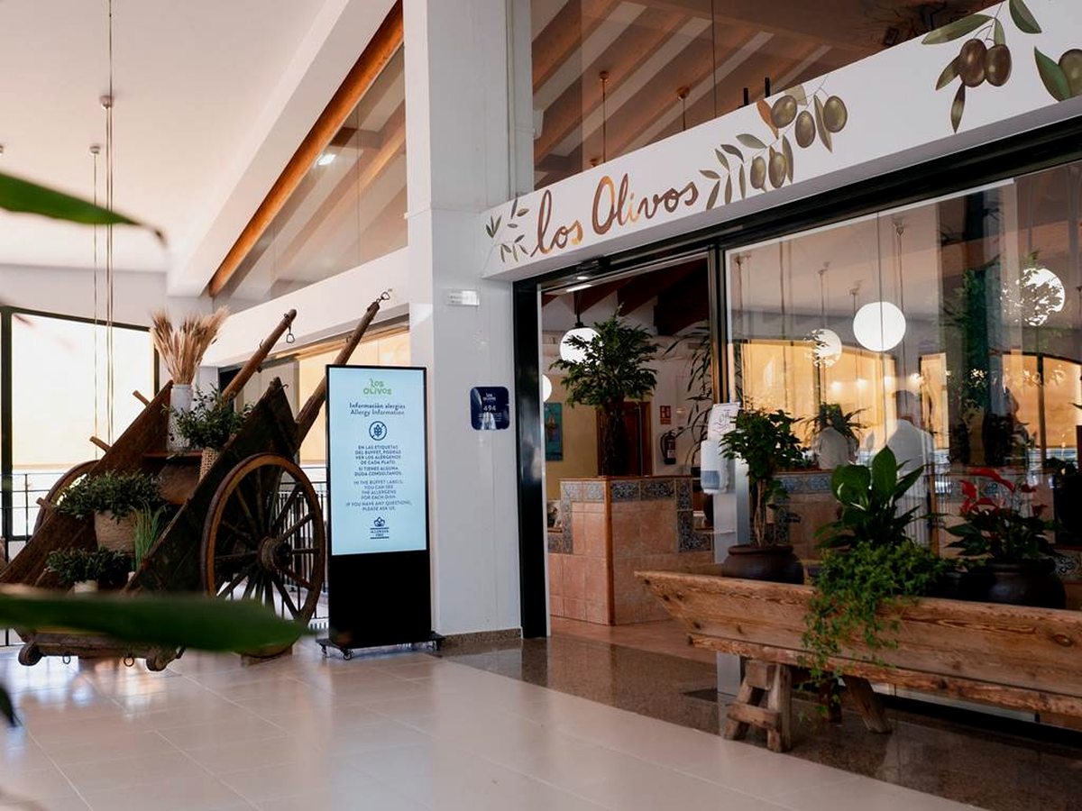 The entrance to Los Olivos restaurant, its name written in script above a glass frontage, with plants, a wooden bench and an old wooden cart in the foyer.