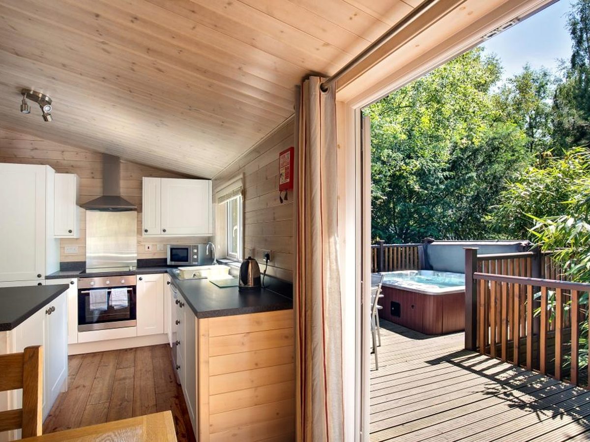 A lodge kitchen with white cabinets, black worktops, an oven, hob, extractor and microwave, opening through wide doors onto a decked terrace.
