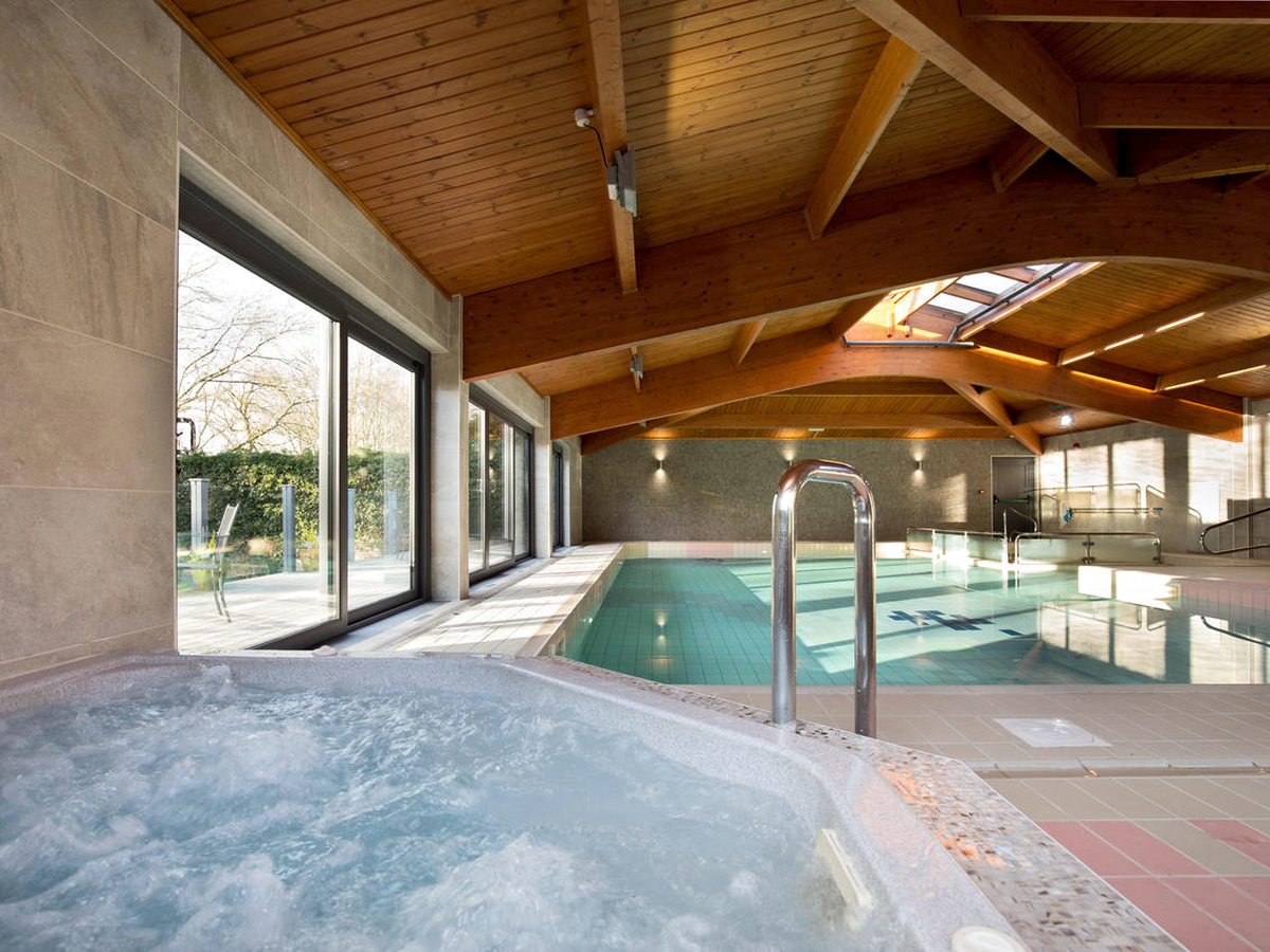 A bubbling built-in spa pool in the corner of the pool hall, with the main swimming pool and glazed doors to the terrace behind it.