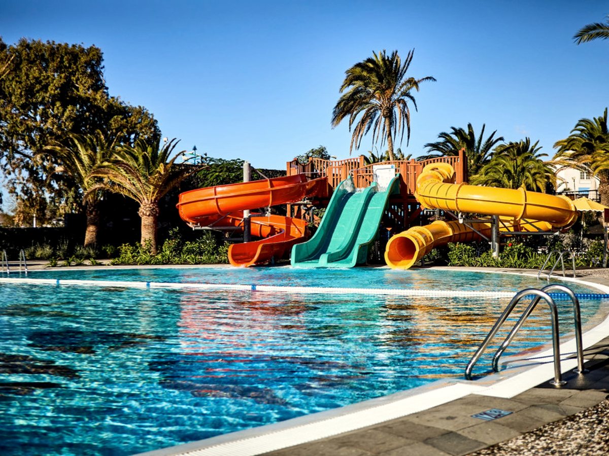Children's pool with red, turquoise and yellow water slides running down into the shallow water, palms behind.
