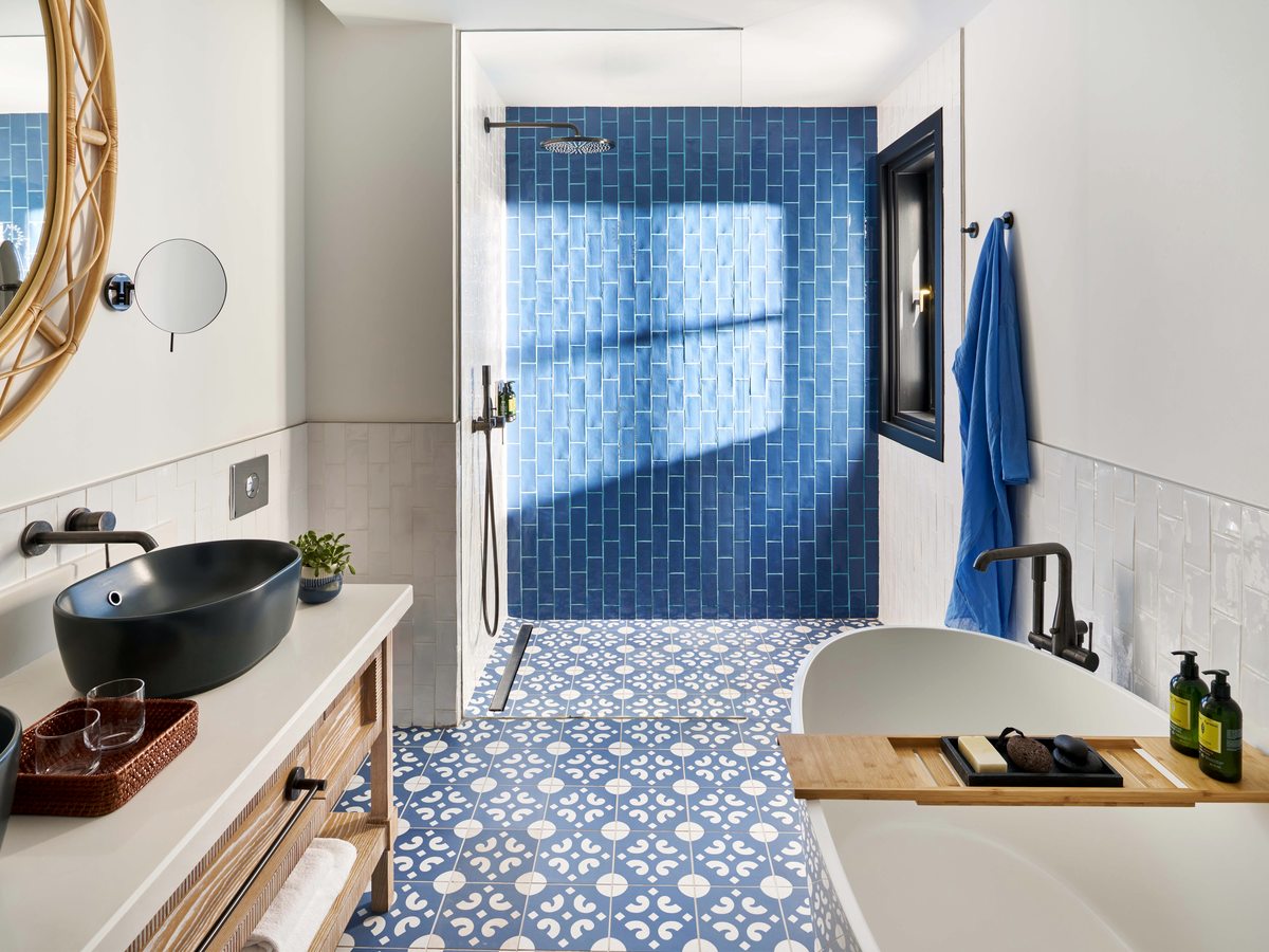 Bathroom with a black stone basin on a wooden vanity, a patterned blue floor, a bath and a blue-tiled walk-in shower.