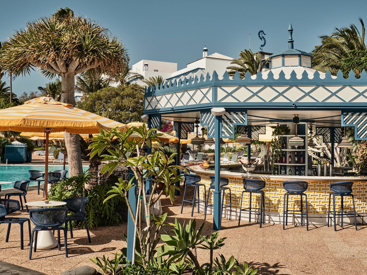 Blue and white octagonal bar pavilion beside the pool, with stools along a yellow-tiled counter and fringed yellow parasols nearby.