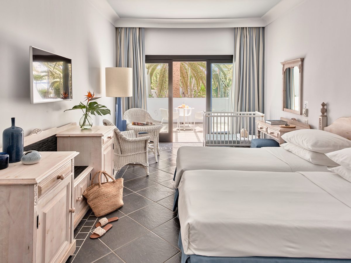 Hotel room with two twin beds pushed together, a white wooden cot beside the window and glass doors onto a furnished terrace.
