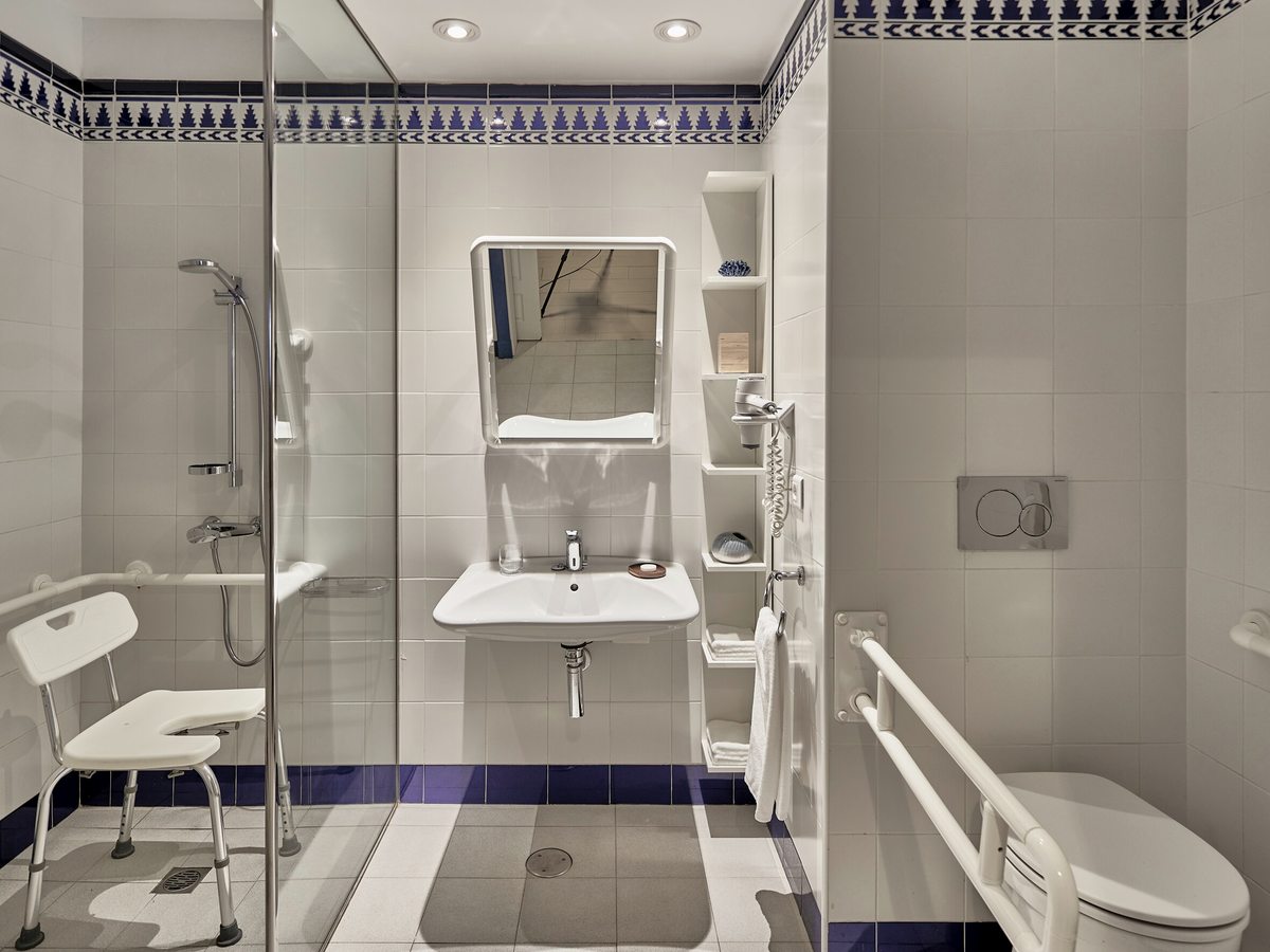 Accessible bathroom with a level-access shower, a folding seat, grab rails beside the toilet and clear space under the basin.