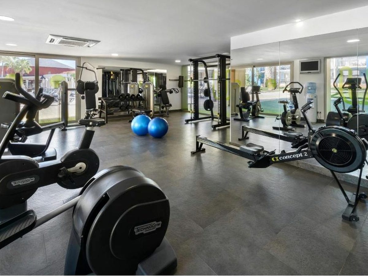 A gym with treadmills, exercise bikes, a rowing machine, free weights and a mirrored wall of resistance machines.