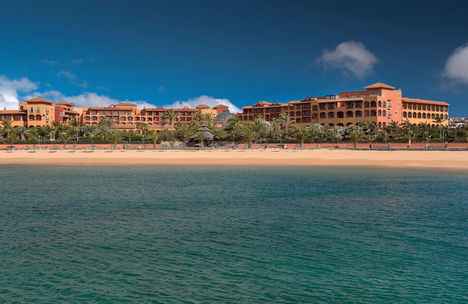 The Sheraton Fuerteventura Beach, Golf & Spa Resort: low-rise Canarian buildings in gardens beside a sheltered sandy cove on Fuerteventura's east coast.