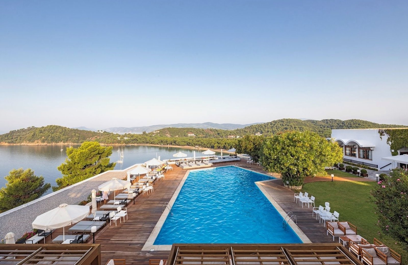 The hotel's freshwater pool on a wooden sun deck, edged with white loungers and parasols, with the pine-wooded bay and its beach beyond.
