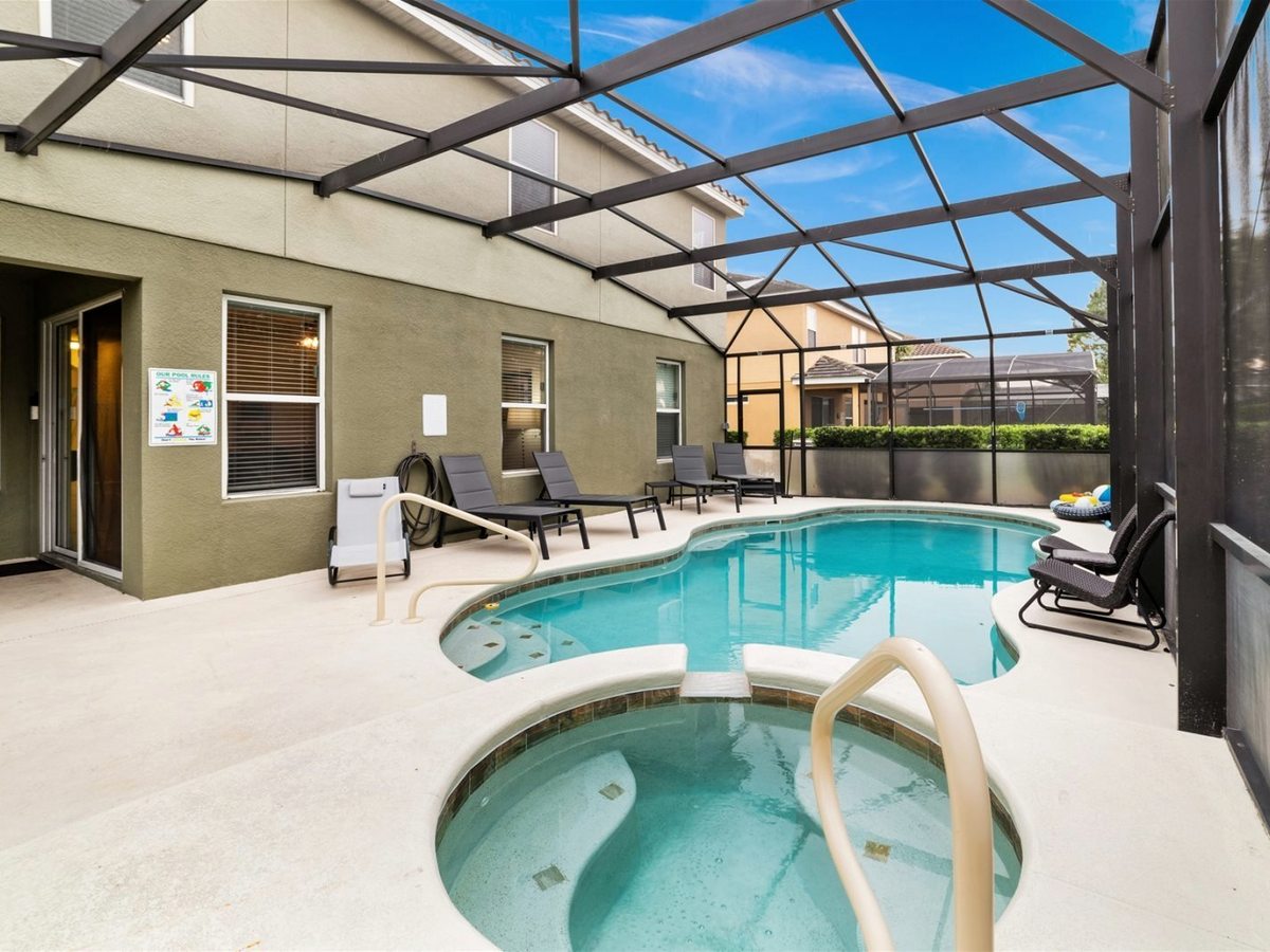 A private rectangular pool with a small round spa, enclosed by a screened patio cage, with sun loungers on the paved deck beside a villa's patio doors.