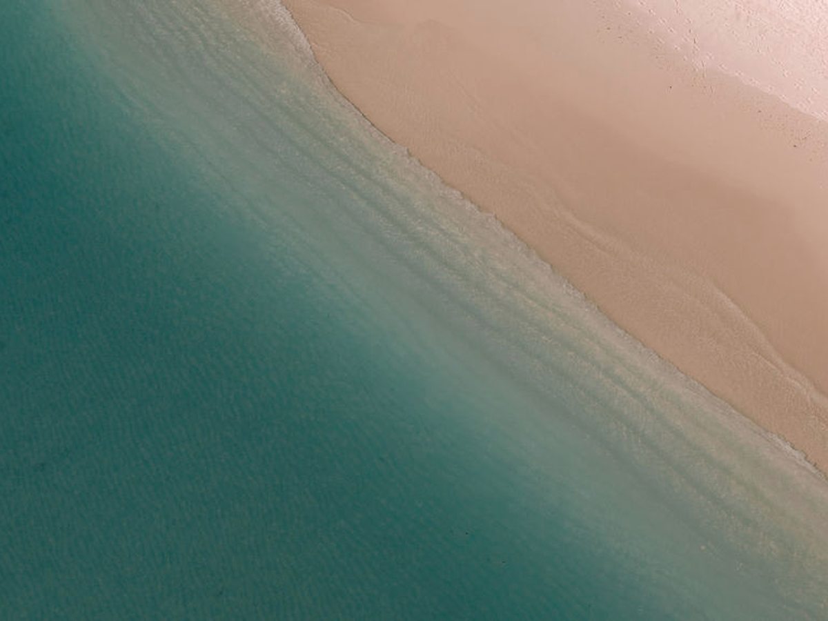 Aerial view of pale turquoise water meeting a broad stretch of white sand.