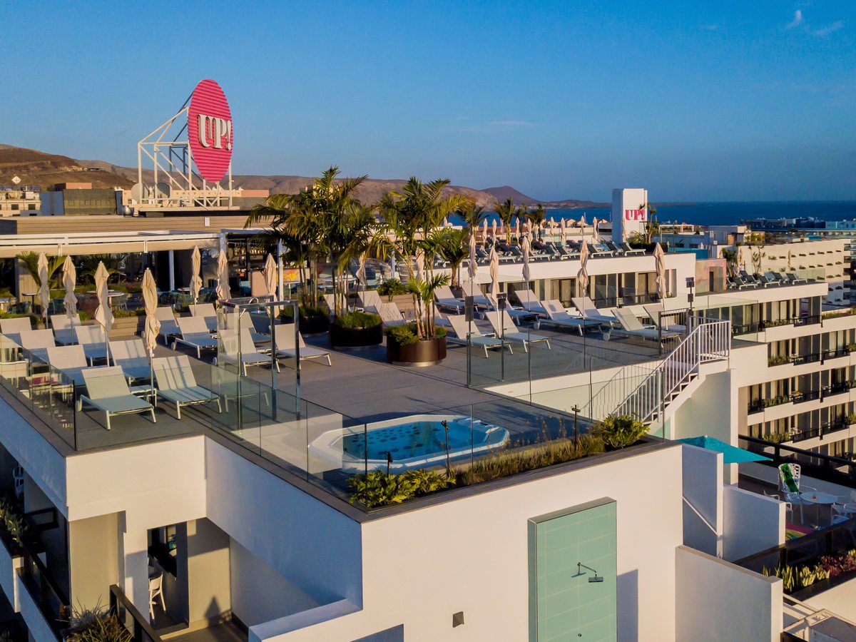 A circular sunken jacuzzi set into a timber roof deck behind glass balustrades, with sun loungers, palms and the sea beyond.