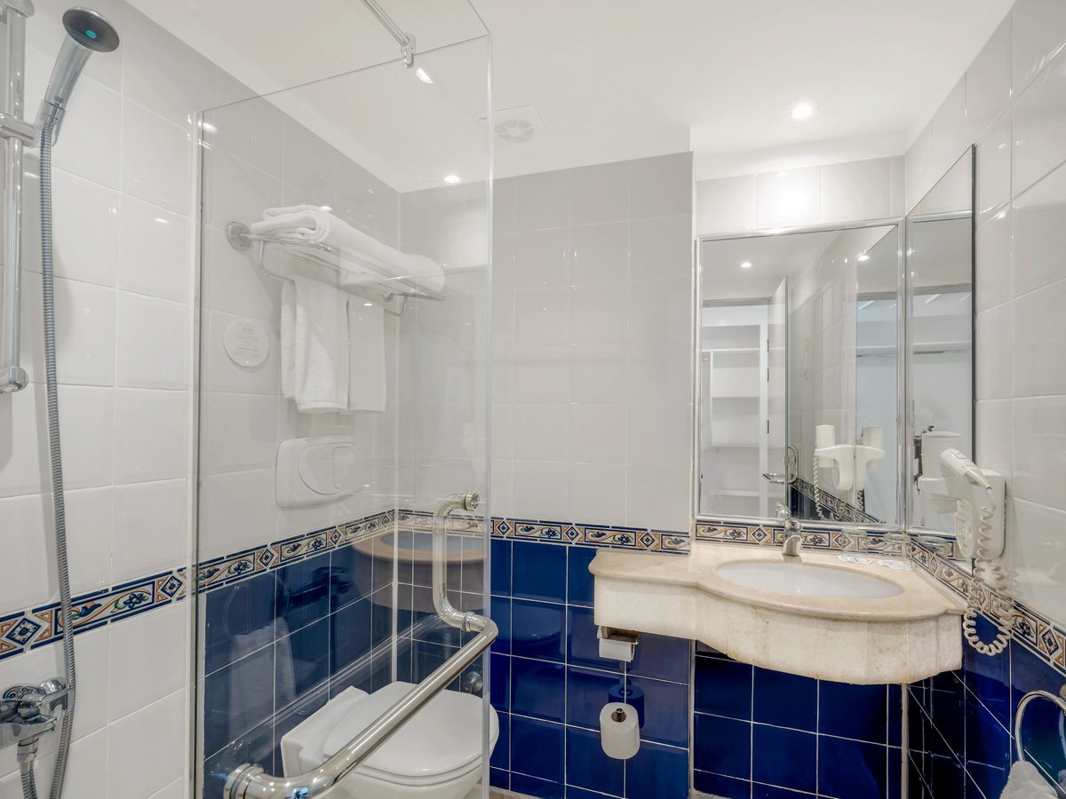 A bathroom with a glass walk-in shower, blue patterned wall tiles, a marble-topped basin and a mirror.
