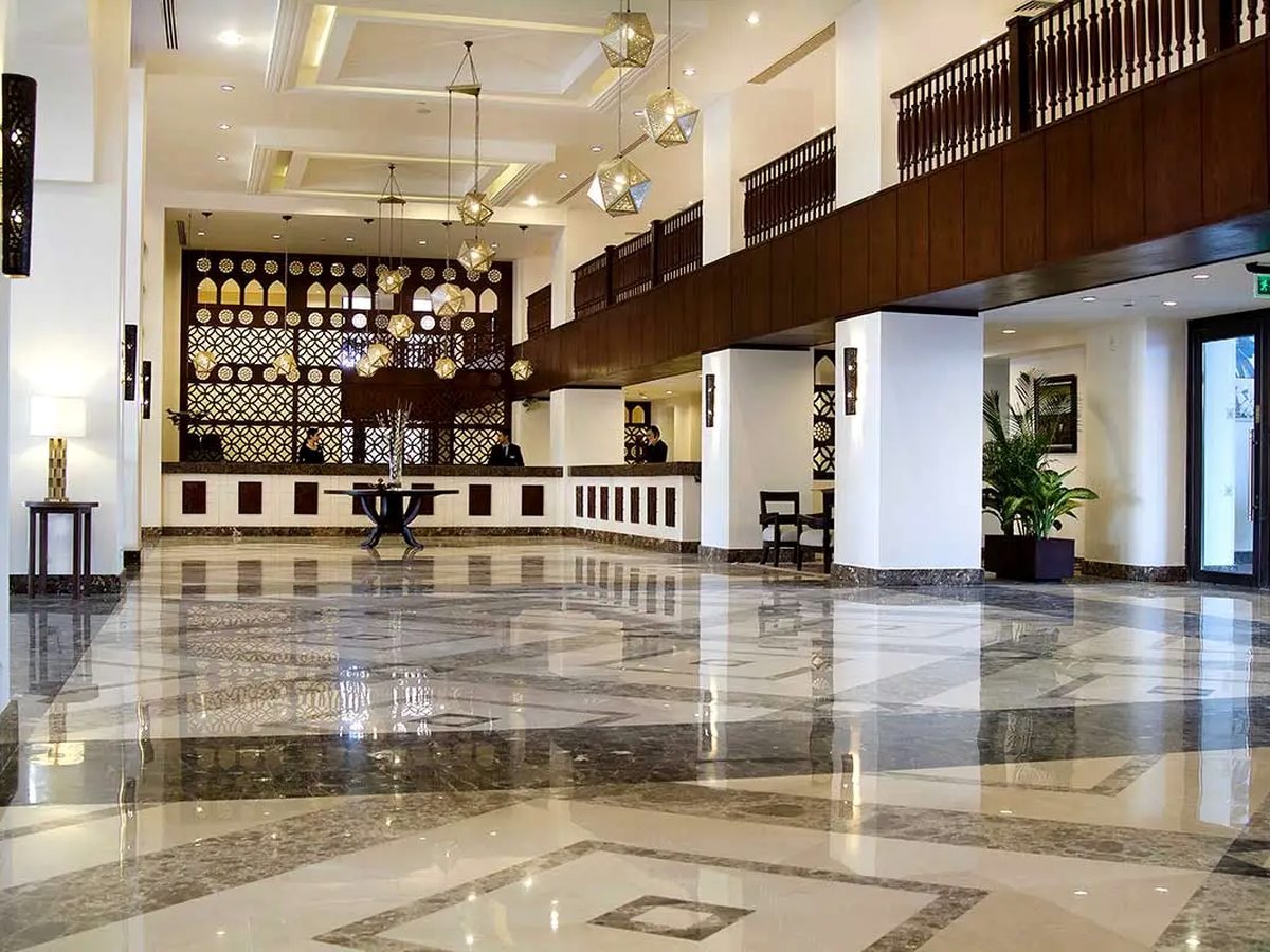 A hotel reception with a long dark-wood desk, a panelled wall of shelves behind it, a polished marble floor and pendant lights.