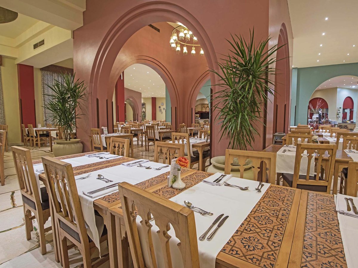A large arched dining hall with wooden chairs, white cloths and patterned table runners, with buffet counters through the archways.