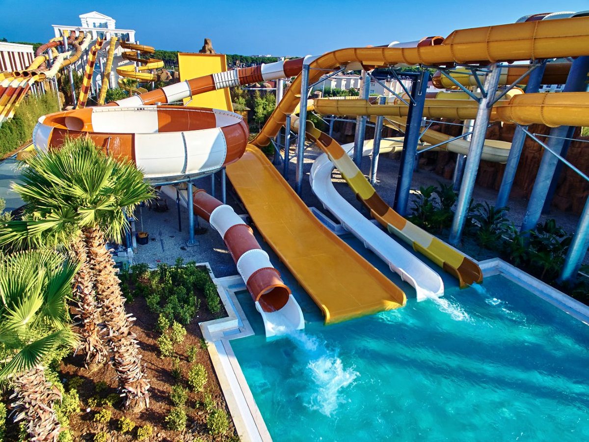 Four water slides running side by side into a turquoise plunge pool, with a large bowl slide and looping tube slides behind.