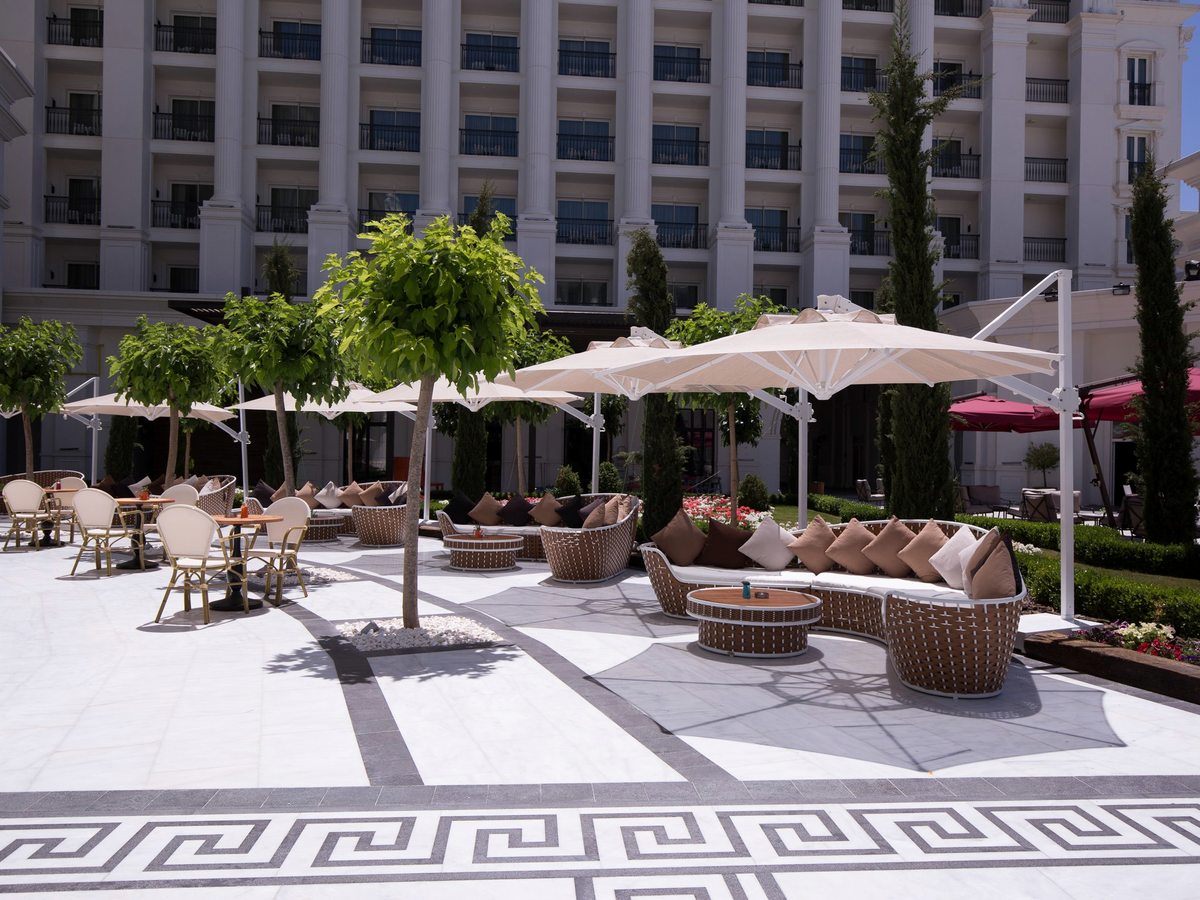 An outdoor terrace paved in patterned marble with white parasols, wicker sofas and small trees, below tiers of guest-room balconies.