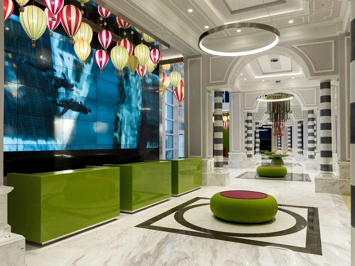 A marble lobby with lime-green reception counters in front of a large video wall, hot-air-balloon lanterns hanging above and green seating beyond.
