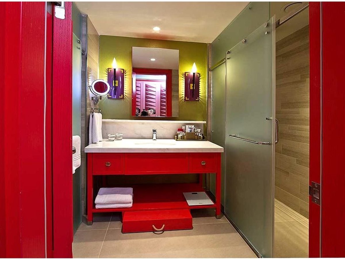 A compact bathroom with a red-framed doorway and vanity, a single basin under a large mirror and folded towels on a shelf.