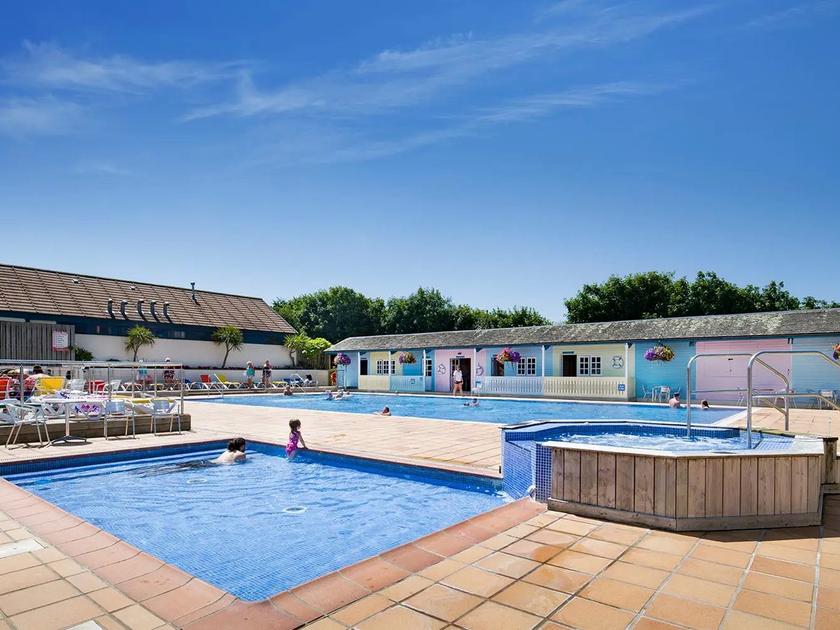 A large rectangular outdoor pool with a smaller shallow pool and a raised jacuzzi in front, edged by pastel-painted changing rooms.