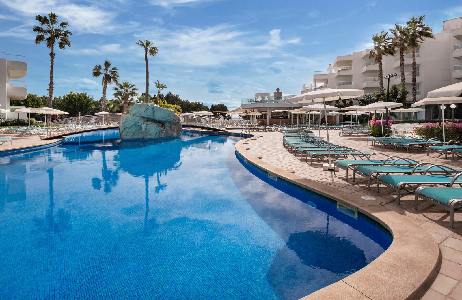 The lagoon-style main pool at Tropic Garden Hotel Apartments, curving round a rock feature past sun loungers and parasols, with the hotel and palms behind.