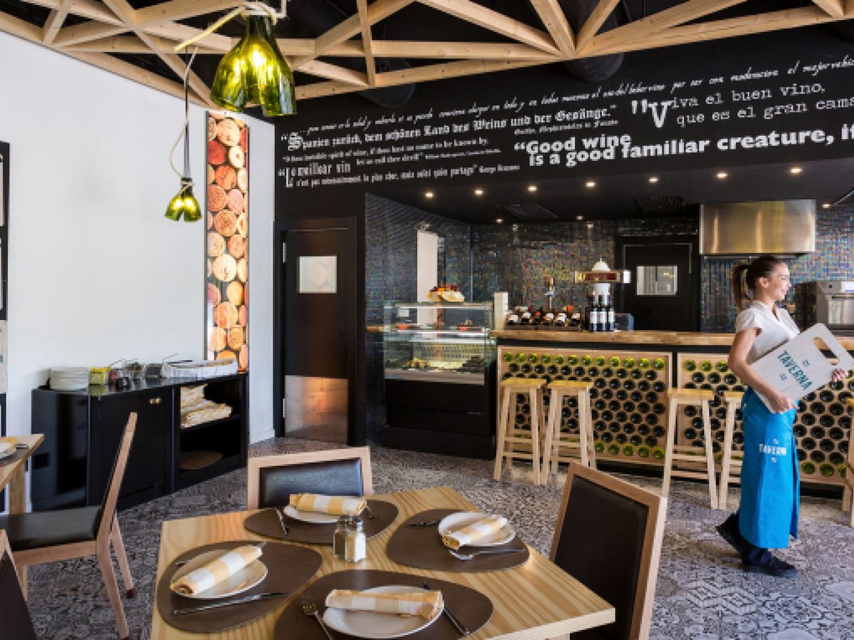 A casual à la carte dining room with set tables, patterned floor tiles and an open service counter with bar stools.