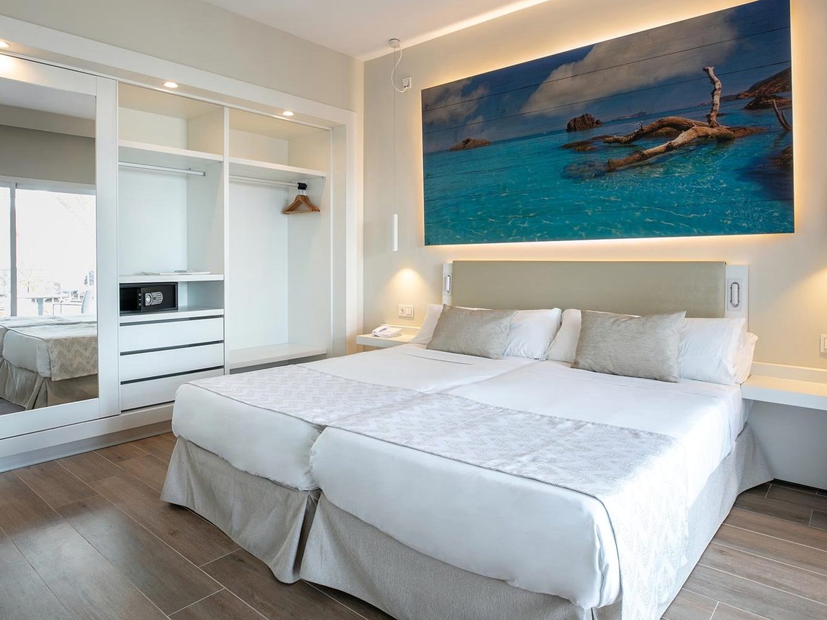 A room with two single beds pushed together under a large sea photograph, with a mirrored wardrobe and bedside reading lights.