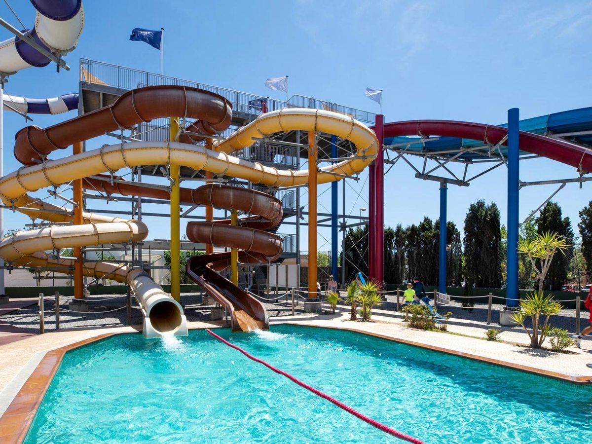 Enclosed tube slides in brown, amber and cream spiralling down a steel tower to a splash pool, with flags flying at the top of the tower.