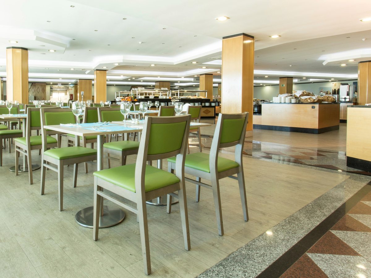 Buffet restaurant with green upholstered chairs at set tables, wood-clad columns and buffet counters along the back wall.