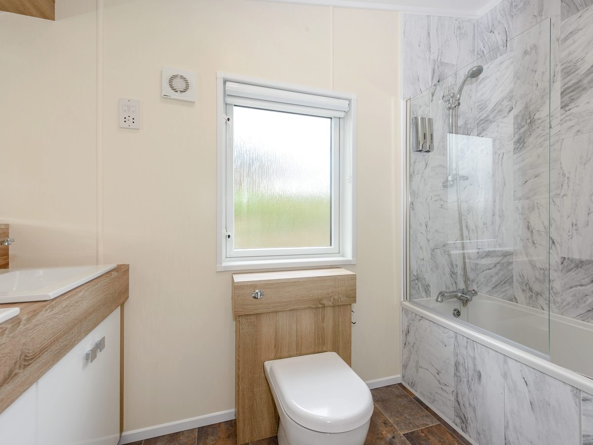 A lodge bathroom with a full-size bath under a wall-mounted shower and glass screen, marble-effect wall panels and a vanity basin.