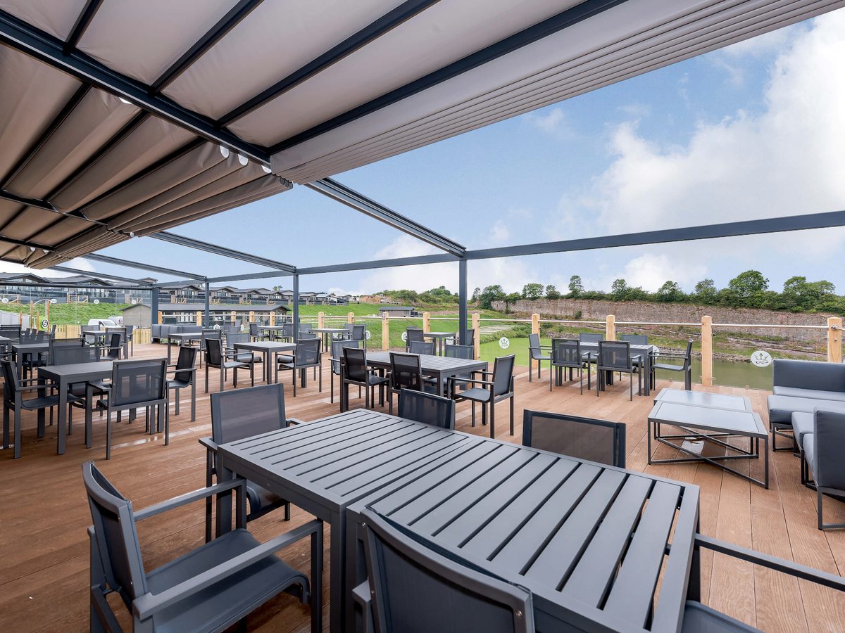 The covered terrace at the Lake House with grey outdoor tables, dining chairs and cushioned lounge seating under a retractable canopy.