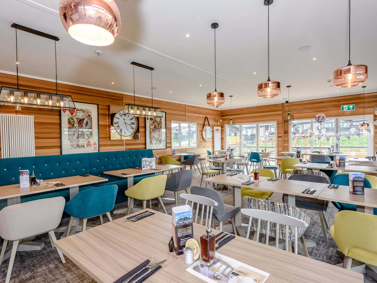 The Lake House dining room with teal banquette seating, pastel dining chairs, timber-panelled walls and copper pendant lights above laid tables.