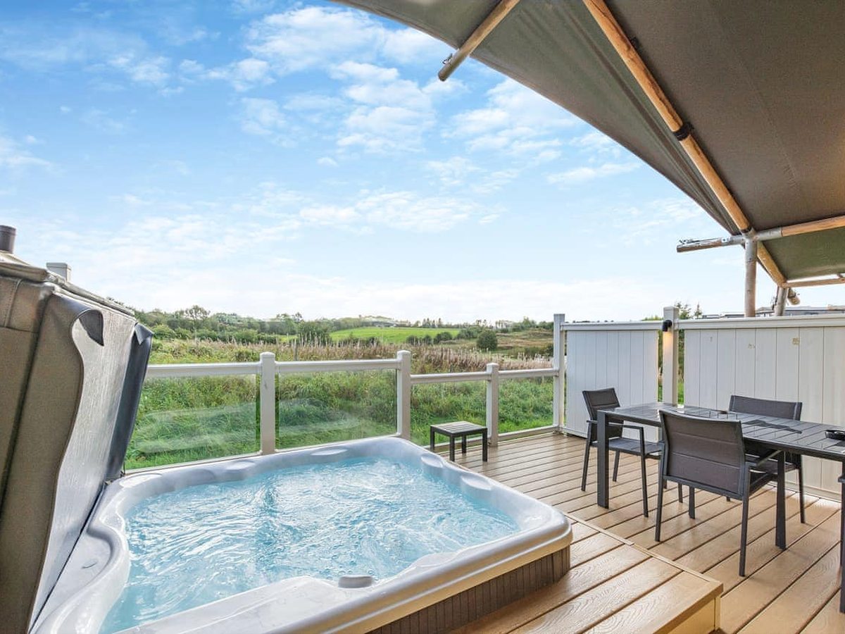 A hot tub on a safari tent's deck under the tent's canopy, with a four-seat dining table and a white balustrade beside it.
