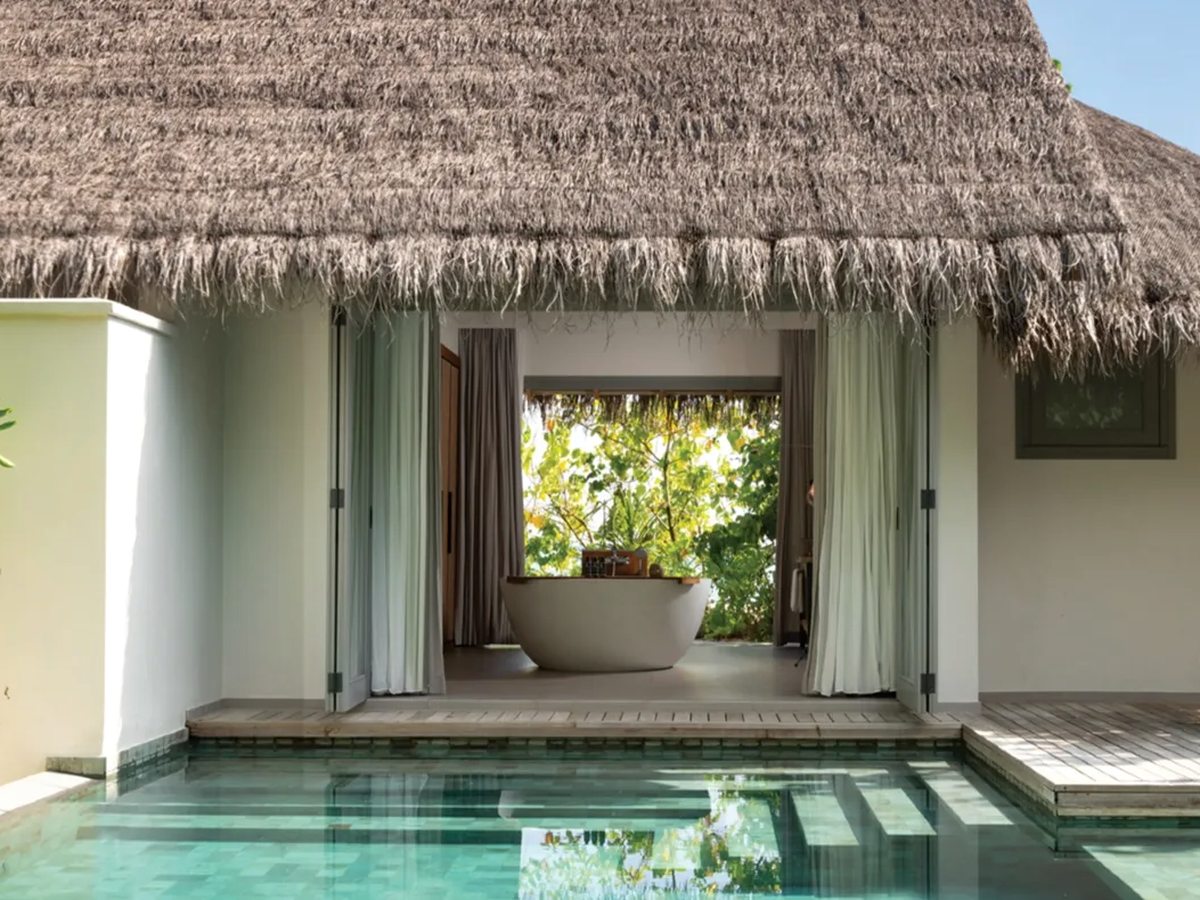 Small green plunge pool along a timber deck, with folding doors open into a villa bathroom and its freestanding bath.